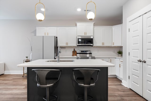 kitchen featuring pendant lighting, sink, appliances with stainless steel finishes, a kitchen island with sink, and white cabinets