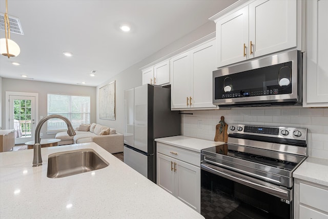 kitchen with appliances with stainless steel finishes, decorative light fixtures, white cabinetry, sink, and light stone counters