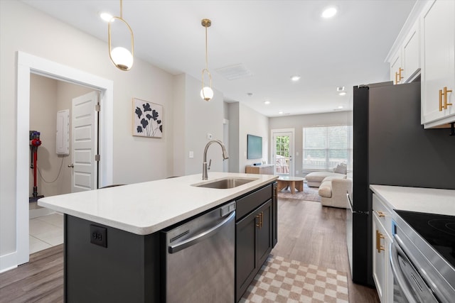 kitchen featuring appliances with stainless steel finishes, sink, white cabinets, hanging light fixtures, and a center island with sink