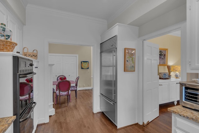 kitchen with white cabinetry, built in refrigerator, crown molding, and hardwood / wood-style flooring