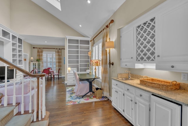 kitchen featuring dark wood-type flooring, sink, white cabinetry, vaulted ceiling, and light stone countertops