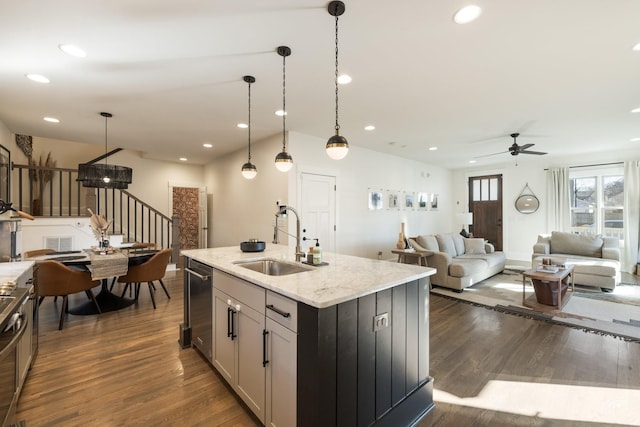 kitchen featuring sink, a kitchen island with sink, dark hardwood / wood-style floors, light stone counters, and decorative light fixtures