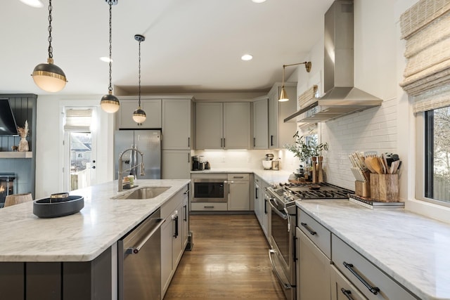 kitchen with extractor fan, light stone counters, decorative light fixtures, stainless steel appliances, and a kitchen island with sink