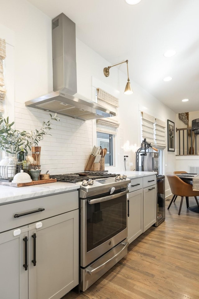 kitchen featuring pendant lighting, light hardwood / wood-style flooring, stainless steel gas stove, island exhaust hood, and beverage cooler