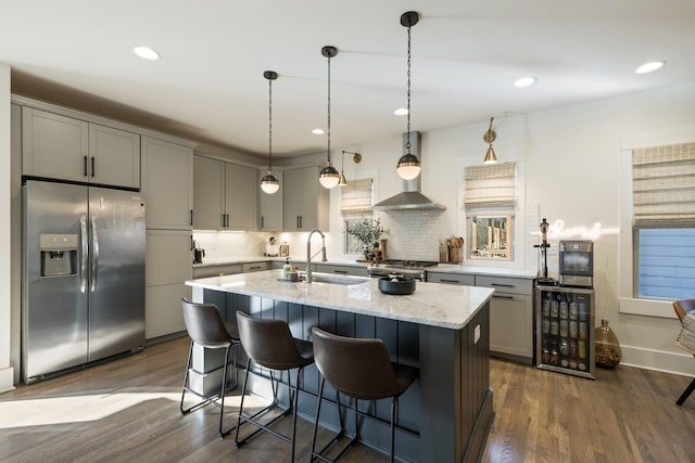 kitchen with sink, light stone counters, a center island with sink, stainless steel appliances, and beverage cooler