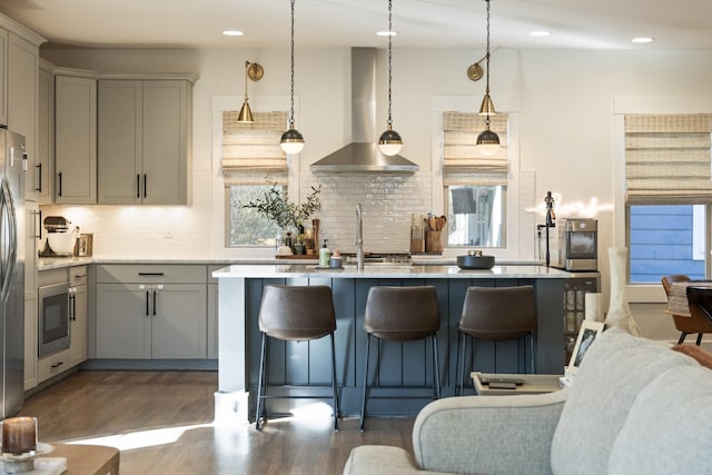 kitchen with pendant lighting, gray cabinetry, light stone countertops, dark wood-type flooring, and wall chimney exhaust hood