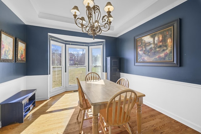 dining room with a notable chandelier, wood-type flooring, ornamental molding, and a raised ceiling