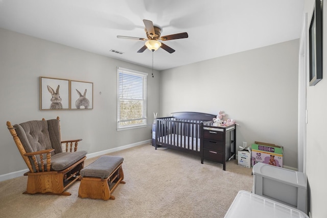 carpeted bedroom featuring a crib and ceiling fan