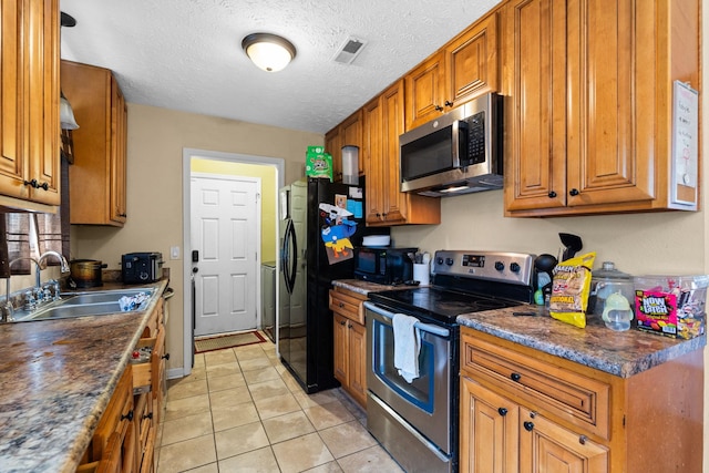 kitchen with sink, light tile patterned floors, dark stone countertops, black appliances, and a textured ceiling