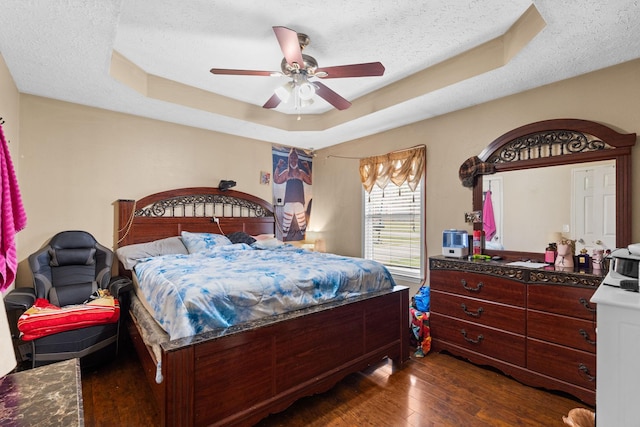 bedroom with ceiling fan, a tray ceiling, dark wood-type flooring, and a textured ceiling