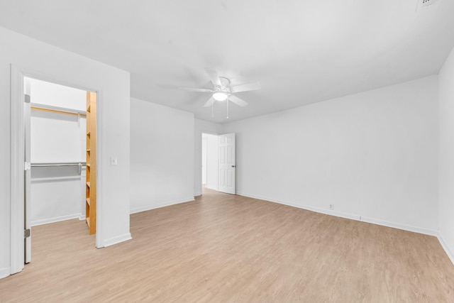 unfurnished bedroom featuring a spacious closet, light hardwood / wood-style floors, a closet, and ceiling fan