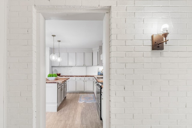 kitchen featuring butcher block countertops, decorative light fixtures, stainless steel range with electric cooktop, backsplash, and light hardwood / wood-style floors