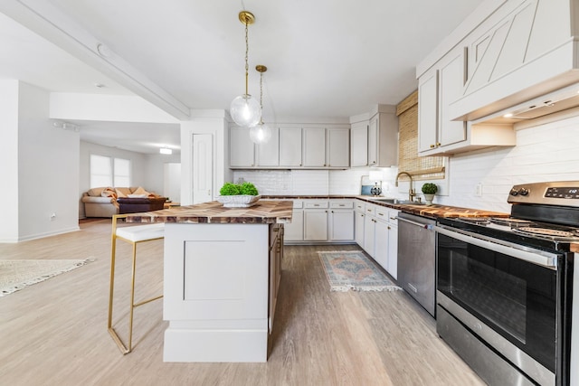 kitchen with butcher block countertops, appliances with stainless steel finishes, hanging light fixtures, a center island, and custom exhaust hood