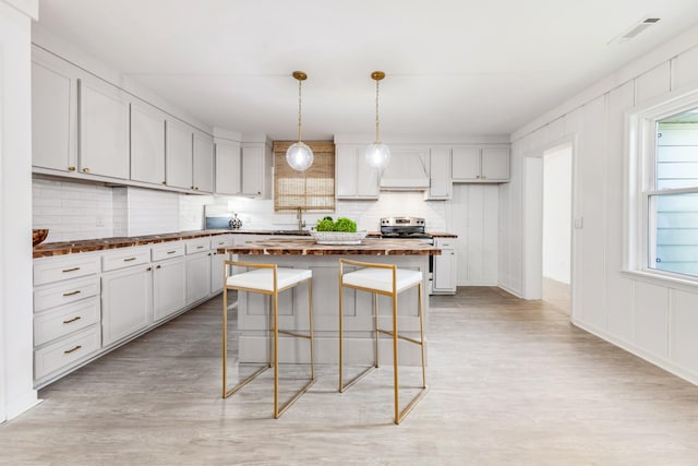 kitchen featuring hanging light fixtures, tasteful backsplash, white cabinets, a kitchen island, and light wood-type flooring