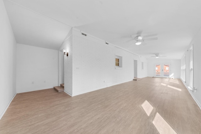 unfurnished living room with french doors, ceiling fan, brick wall, and light hardwood / wood-style flooring