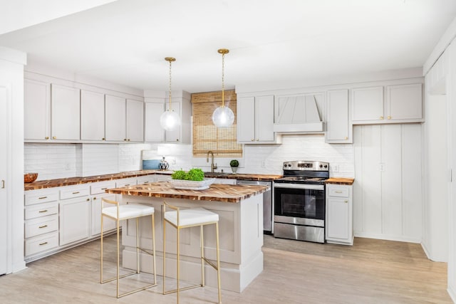 kitchen with a kitchen island, appliances with stainless steel finishes, white cabinetry, decorative backsplash, and custom range hood