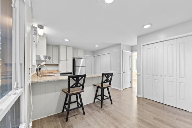 kitchen with stainless steel refrigerator, sink, a kitchen breakfast bar, light hardwood / wood-style floors, and light stone countertops