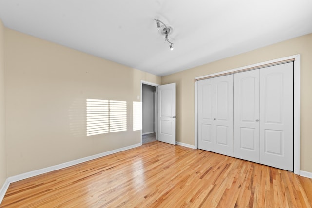 unfurnished bedroom with light hardwood / wood-style flooring, a closet, and track lighting