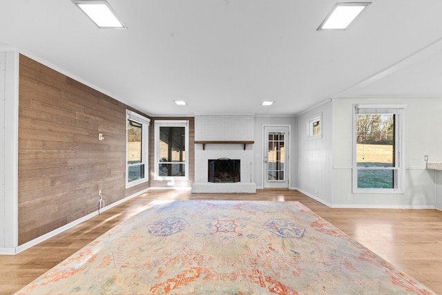 unfurnished living room featuring ornamental molding, light wood-type flooring, wooden walls, and a fireplace