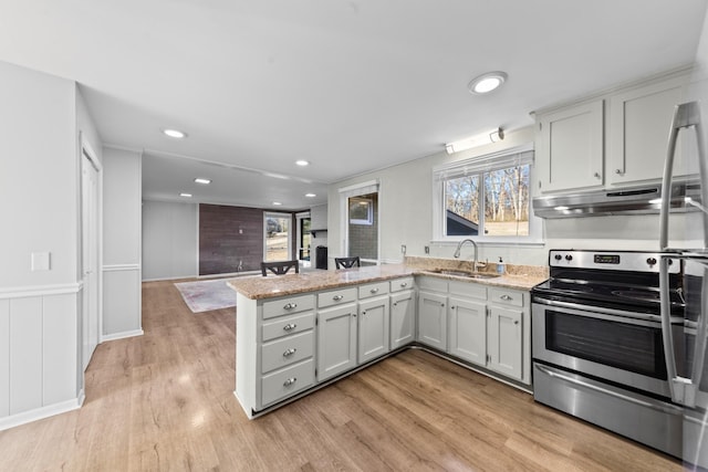 kitchen with sink, stainless steel electric range, light stone counters, kitchen peninsula, and light wood-type flooring