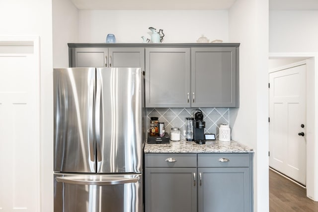 kitchen with stainless steel refrigerator, light stone countertops, decorative backsplash, and gray cabinetry