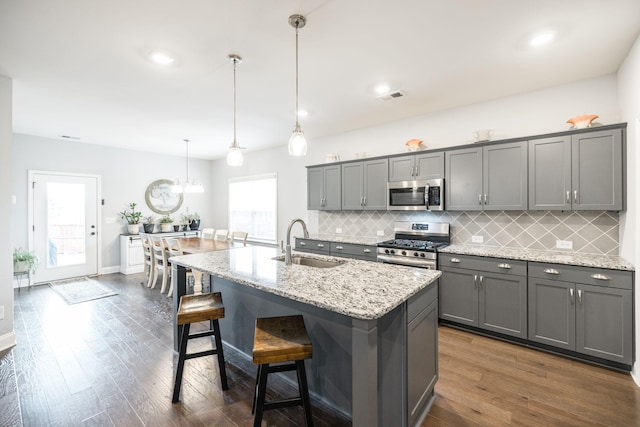 kitchen with pendant lighting, sink, gray cabinets, appliances with stainless steel finishes, and a center island with sink