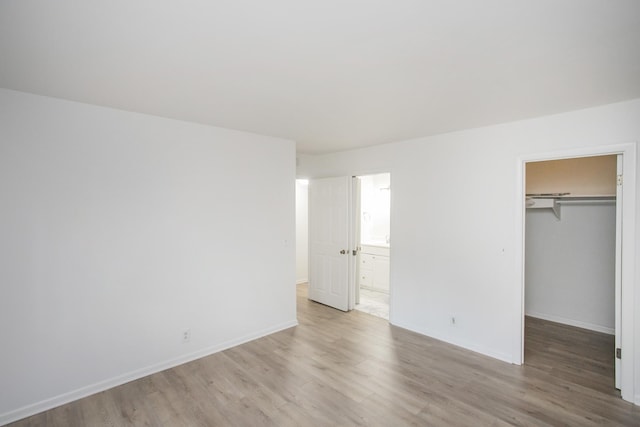 unfurnished bedroom featuring a closet, a spacious closet, ensuite bathroom, and light hardwood / wood-style flooring