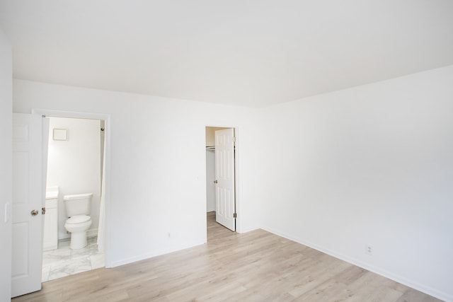 unfurnished bedroom with ensuite bath, a walk in closet, a closet, and light wood-type flooring