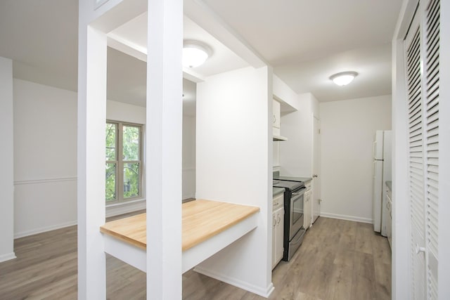 kitchen featuring white cabinetry, light hardwood / wood-style flooring, white refrigerator, stainless steel electric stove, and wall chimney range hood