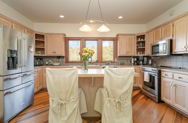 kitchen featuring a kitchen island, pendant lighting, high end appliances, light hardwood / wood-style floors, and light brown cabinets