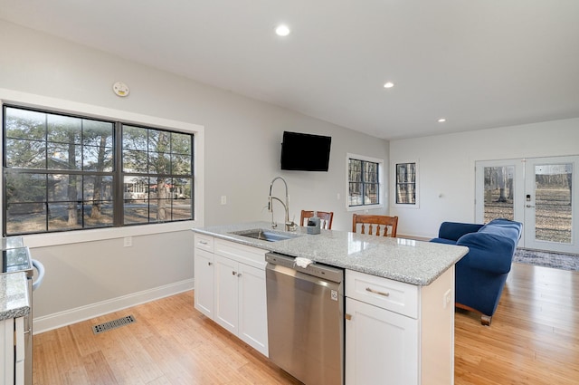 kitchen featuring sink, dishwasher, light stone countertops, white cabinets, and a center island with sink