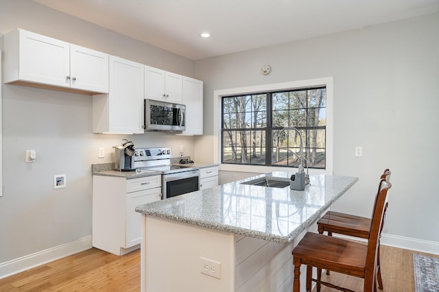 kitchen with stainless steel appliances, a center island with sink, white cabinets, and light stone counters