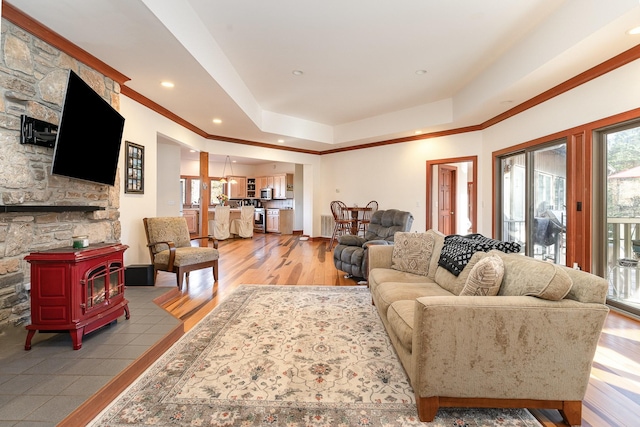 living room with light hardwood / wood-style flooring, ornamental molding, a raised ceiling, and a wood stove