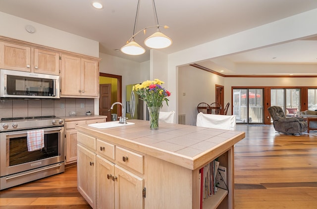 kitchen featuring light brown cabinetry, sink, tile counters, stainless steel appliances, and a kitchen island with sink