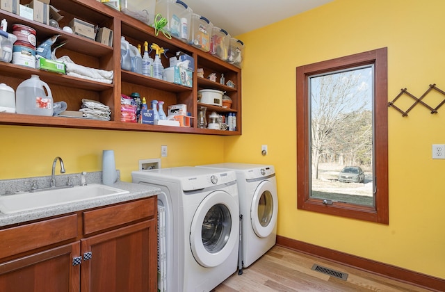 washroom with washer and dryer, sink, cabinets, and light wood-type flooring