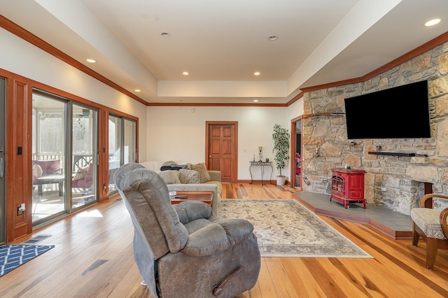 living room with a wood stove, a tray ceiling, ornamental molding, and light wood-type flooring