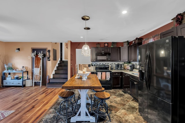 kitchen featuring dark brown cabinetry, wood-type flooring, hanging light fixtures, decorative backsplash, and black appliances