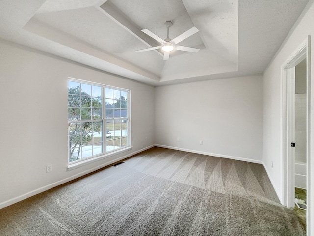 spare room with a raised ceiling, carpet, and ceiling fan