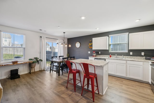 kitchen featuring a kitchen island, decorative light fixtures, sink, white cabinets, and light stone countertops