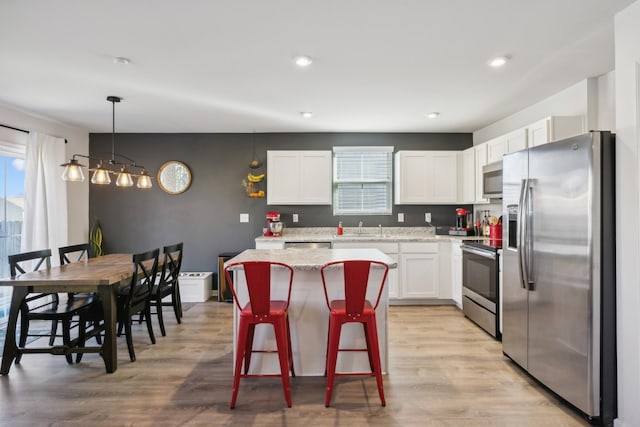 kitchen with pendant lighting, white cabinetry, stainless steel appliances, a kitchen breakfast bar, and a center island