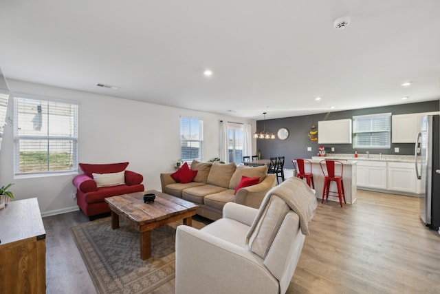 living room with a chandelier, light hardwood / wood-style floors, and a wealth of natural light