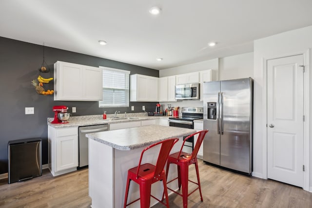 kitchen with stainless steel appliances, white cabinetry, a kitchen island, and a kitchen bar