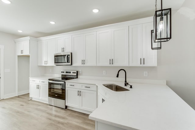 kitchen featuring sink, light hardwood / wood-style flooring, appliances with stainless steel finishes, white cabinetry, and hanging light fixtures