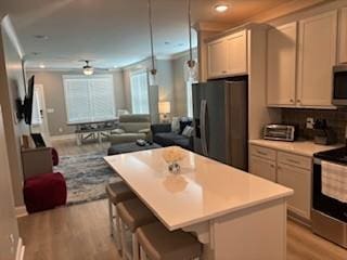 kitchen with a breakfast bar area, appliances with stainless steel finishes, hanging light fixtures, a kitchen island, and light wood-type flooring