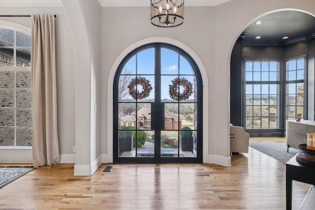 entryway with crown molding, a chandelier, and light wood-type flooring