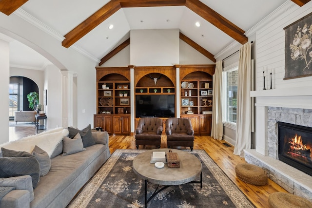 living room featuring beam ceiling, a stone fireplace, and light wood-type flooring