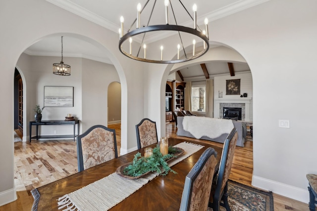 dining space featuring lofted ceiling with beams, crown molding, a notable chandelier, and light hardwood / wood-style floors