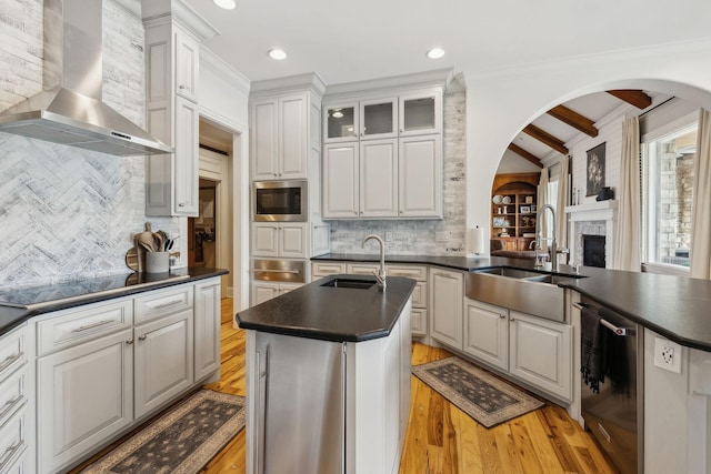 kitchen featuring wall chimney range hood, sink, white cabinetry, a center island with sink, and black electric cooktop