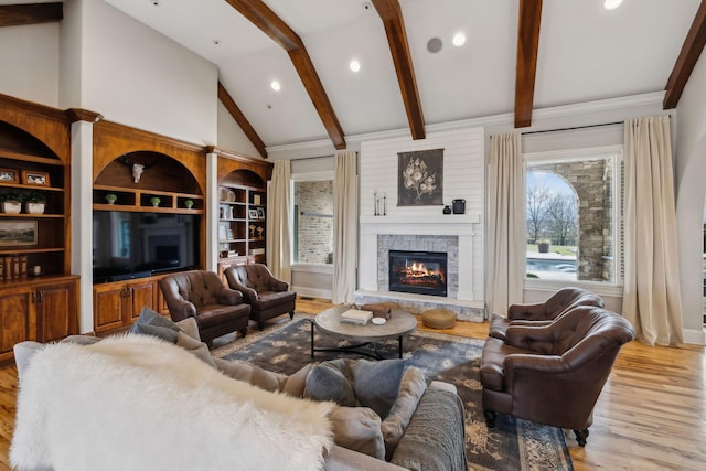 living room featuring beam ceiling, plenty of natural light, a stone fireplace, and light wood-type flooring