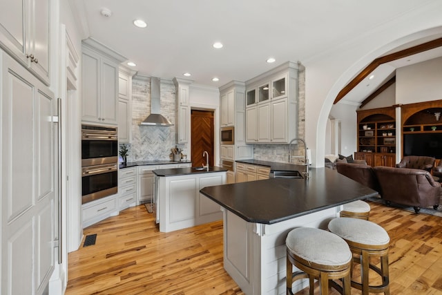 kitchen featuring wall chimney exhaust hood, sink, appliances with stainless steel finishes, a kitchen breakfast bar, and kitchen peninsula